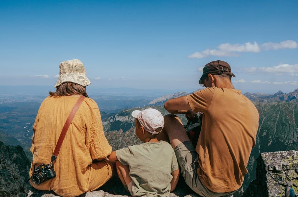 Family sitting on a rock, enjoying a panoramic view of the Tatra Mountains under clear blue skies.