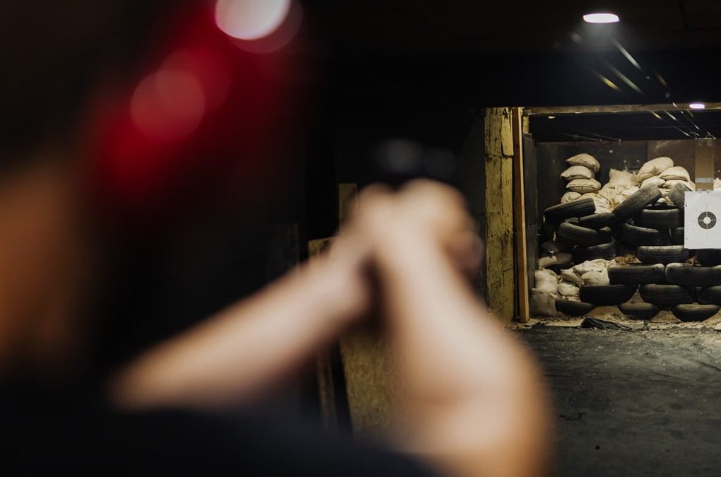 A person at an indoor shooting range aims at a stacked tire target.