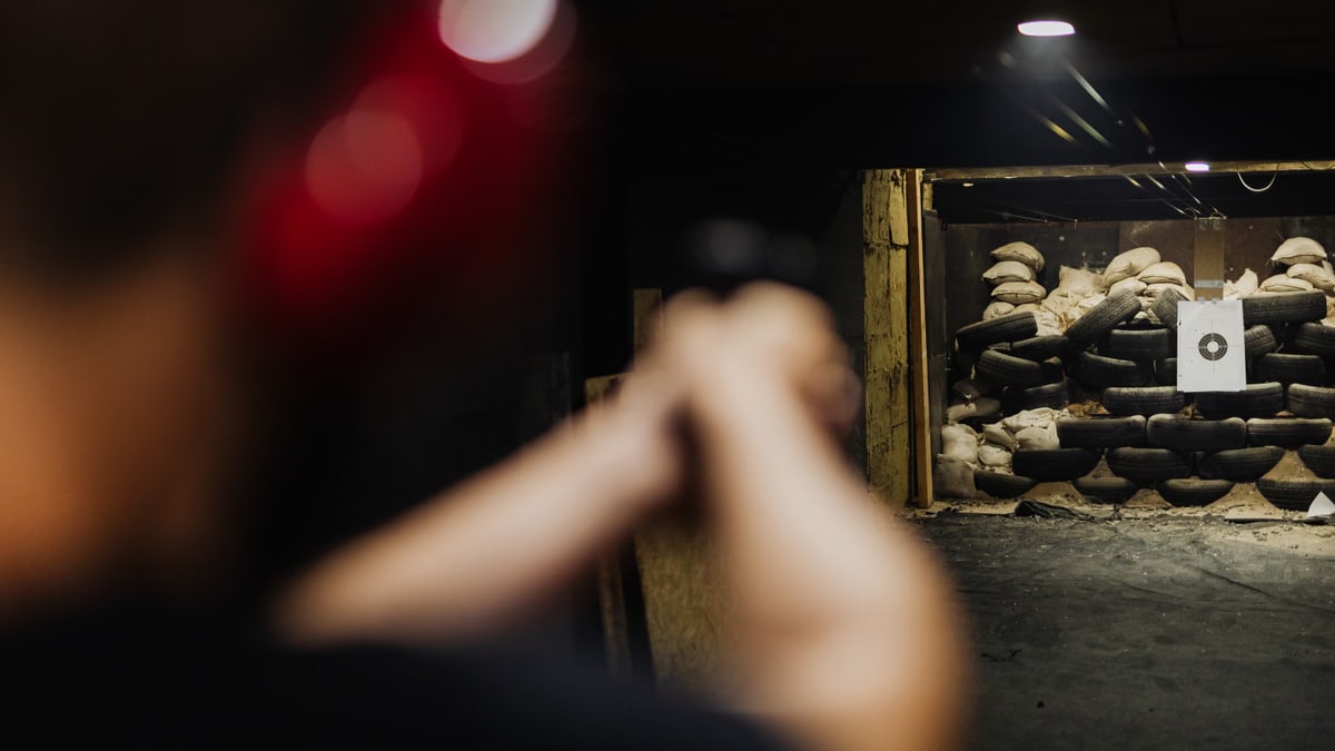 A person at an indoor shooting range aims at a stacked tire target.